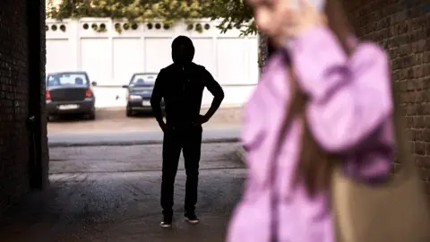 Ilustračná fotografia: Žena kráča osamote ulicou, zatiaľ čo v pozadí stojí neznámy muž. Pocit, že nás niekto sleduje, môže vzniknúť aj na základe nenápadných podnetov, ktoré mozog vyhodnotí ako možnú prítomnosť iného človeka. Niekedy však môže ísť iba o mylný dojem. Foto: Shakirov Albert / Shutterstock
